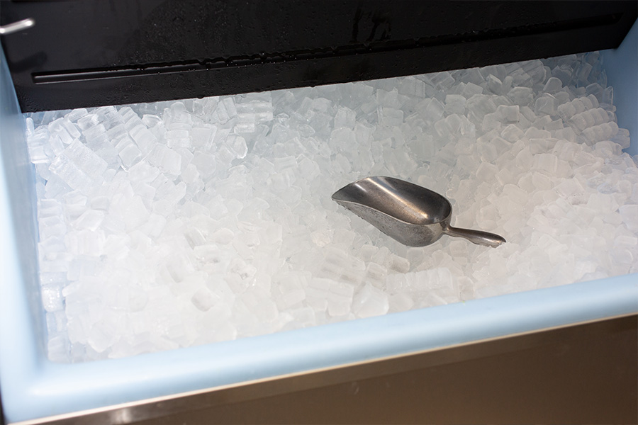 Commercial ice machine filled with ice and ice scoop sitting on top of the ice.